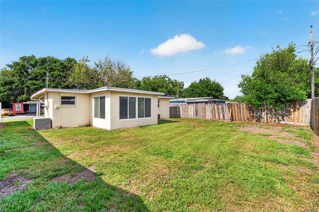 The backyard of a single-story house features a lawn, a wooden fence, and trees — 10246 117TH DRIVE, LARGO, FL