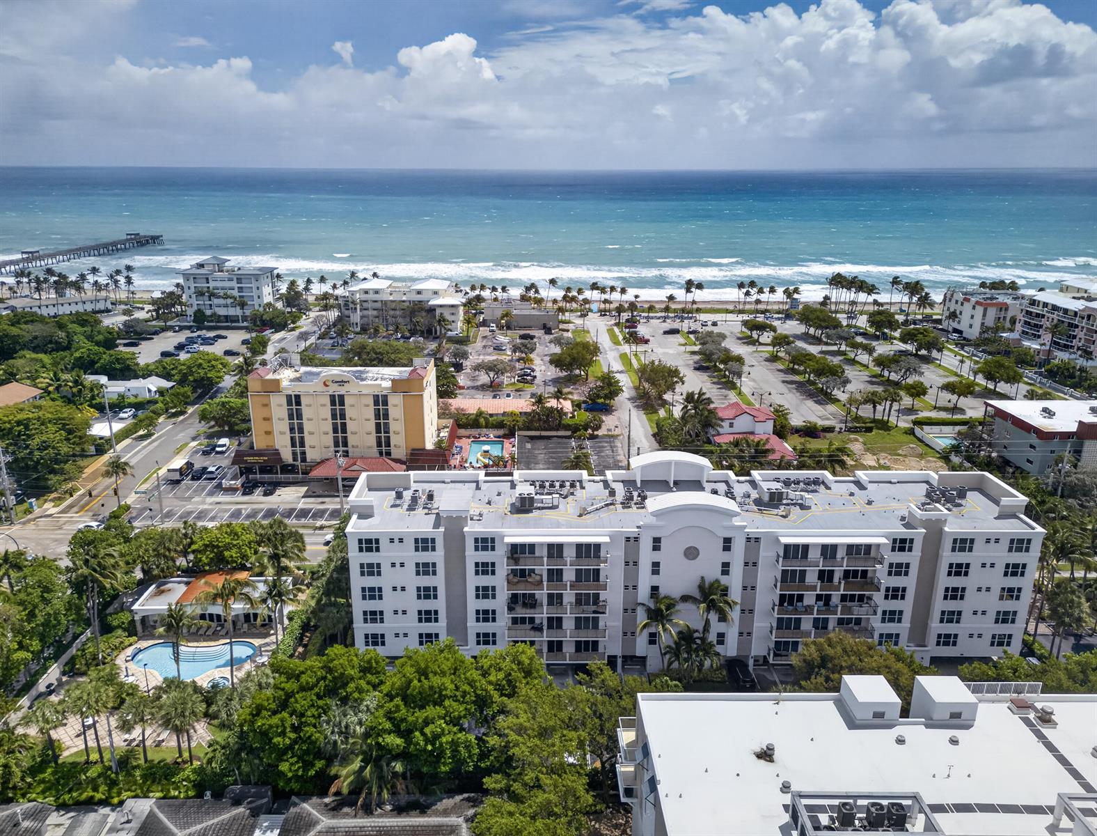 An aerial view shows a multi-story white apartment building near a beach and parking lot — 101 SE 20th Avenue # 201, Deerfield Beach FL 33441, DEERFIELD BEACH, FL