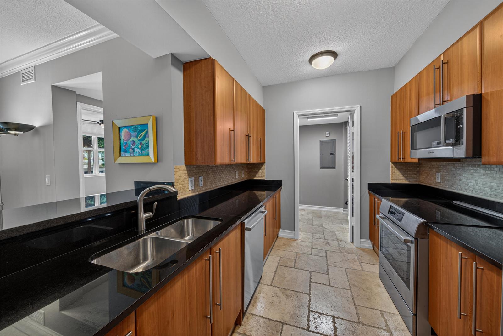 A galley kitchen features wood cabinets, black countertops, stainless steel appliances, and stone tile flooring — 101 SE 20th Avenue # 201, Deerfield Beach FL 33441, DEERFIELD BEACH, FL