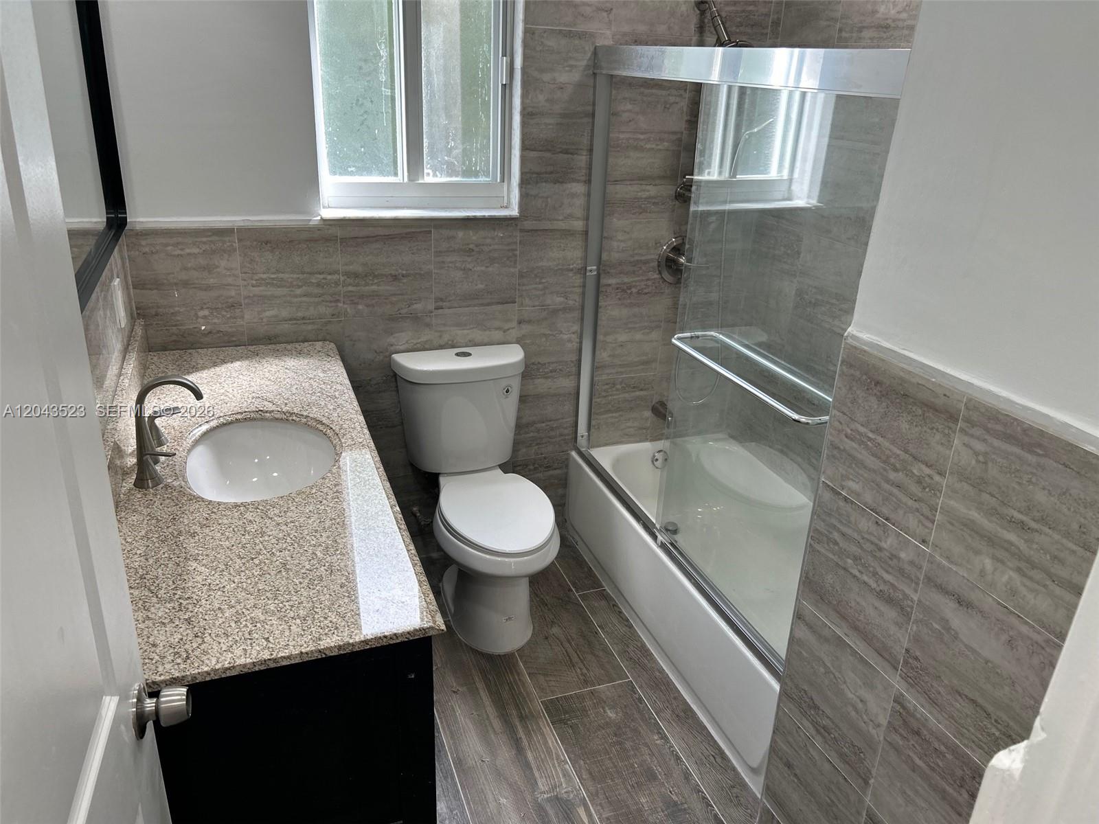 A bathroom features a granite vanity, a white toilet, and a tiled shower-tub combination — 261 NW 49th St # A, Miami FL 33127, MIAMI, FL