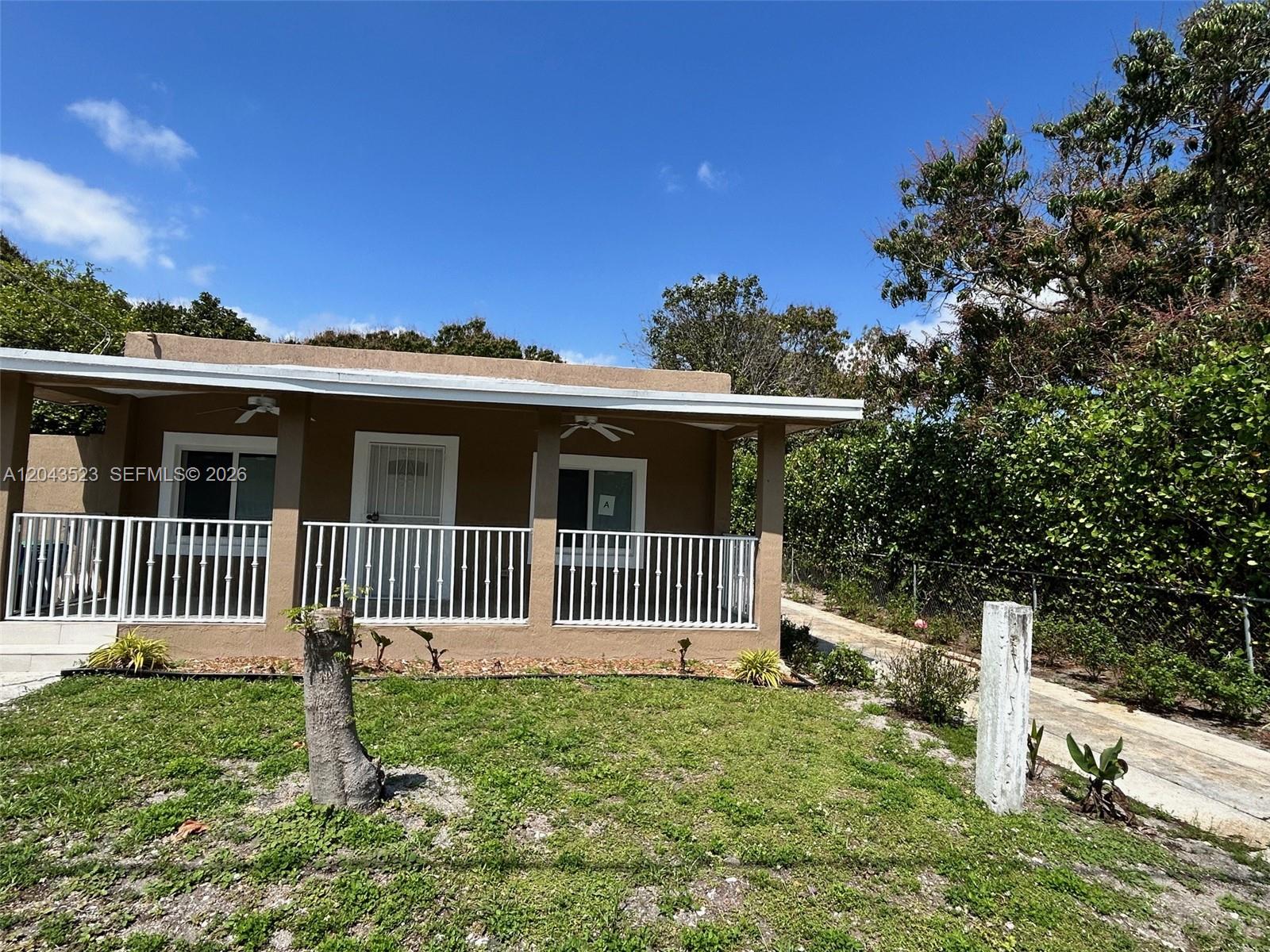 A tan, single-story house features a covered front porch with white railings and a lawn — 261 NW 49th St # A, Miami FL 33127, MIAMI, FL