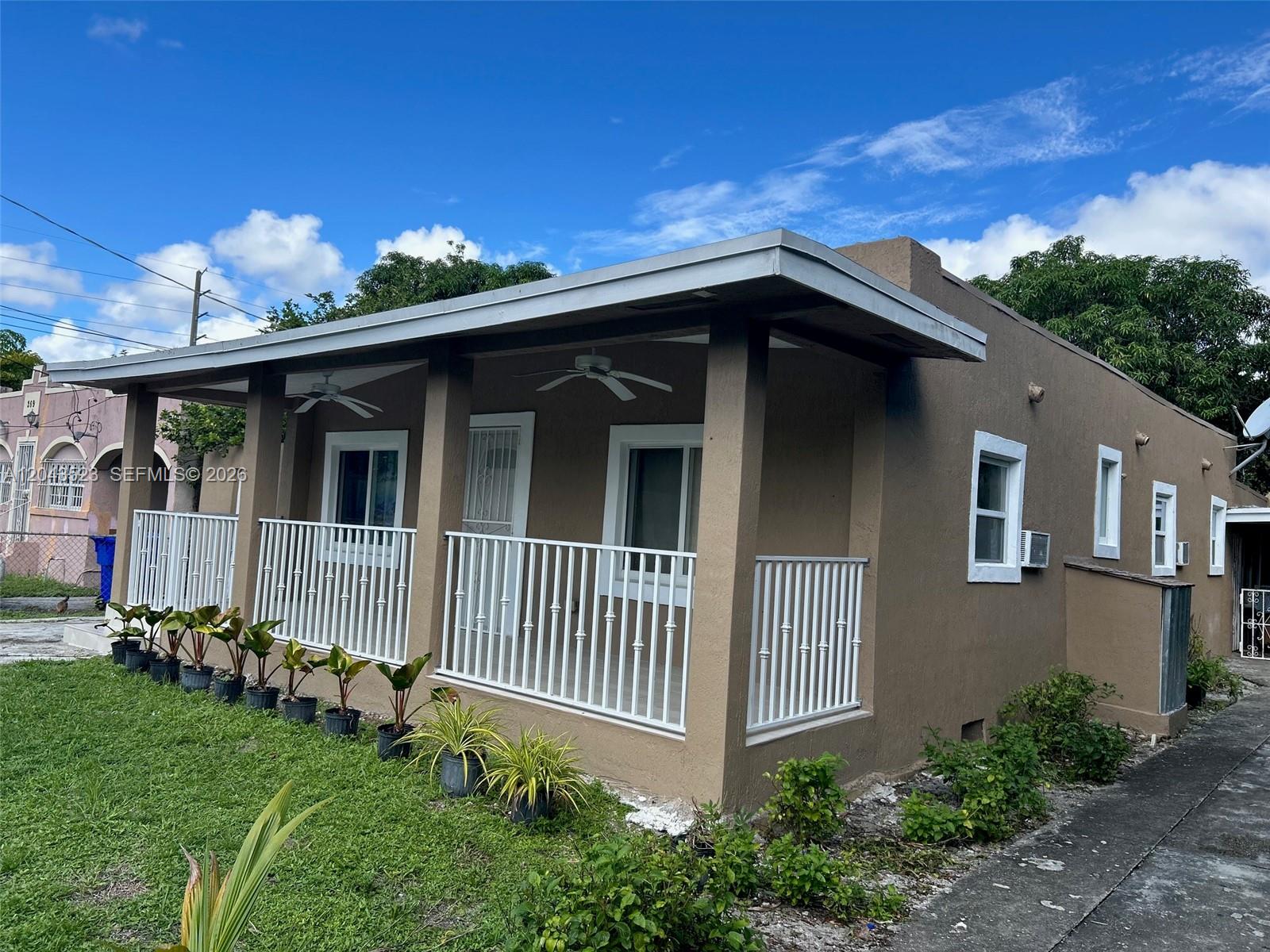 A tan, single-story house features a covered front porch with white railings and ceiling fans — 261 NW 49th St # A, Miami FL 33127, MIAMI, FL