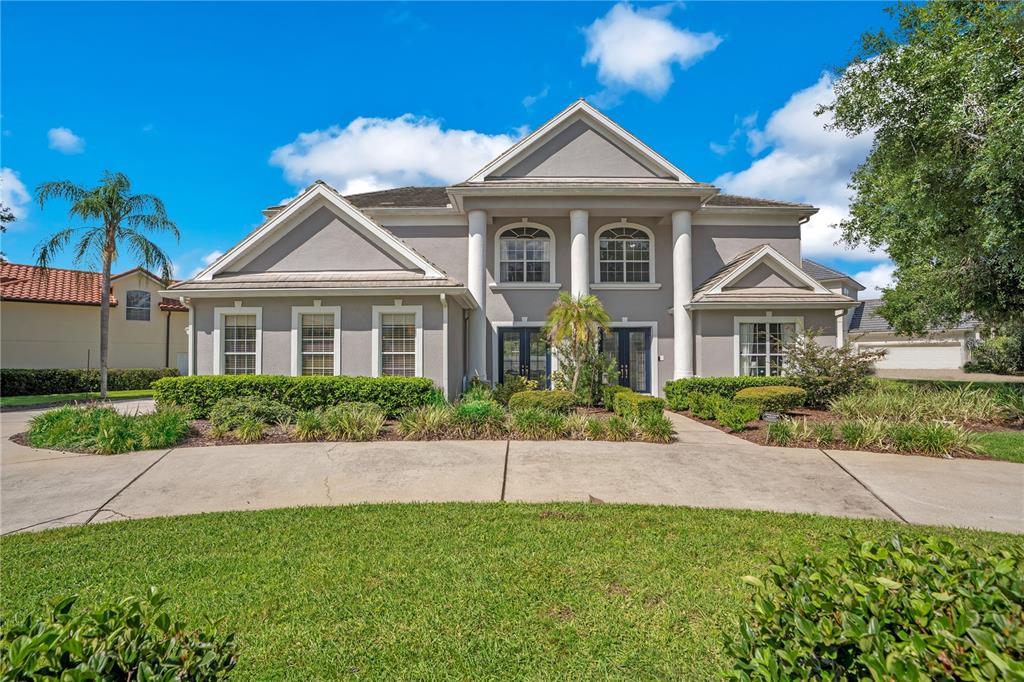 A two-story gray house with a columned entryway and a large concrete driveway — 10760 EMERALD CHASE DRIVE, ORLANDO, FL