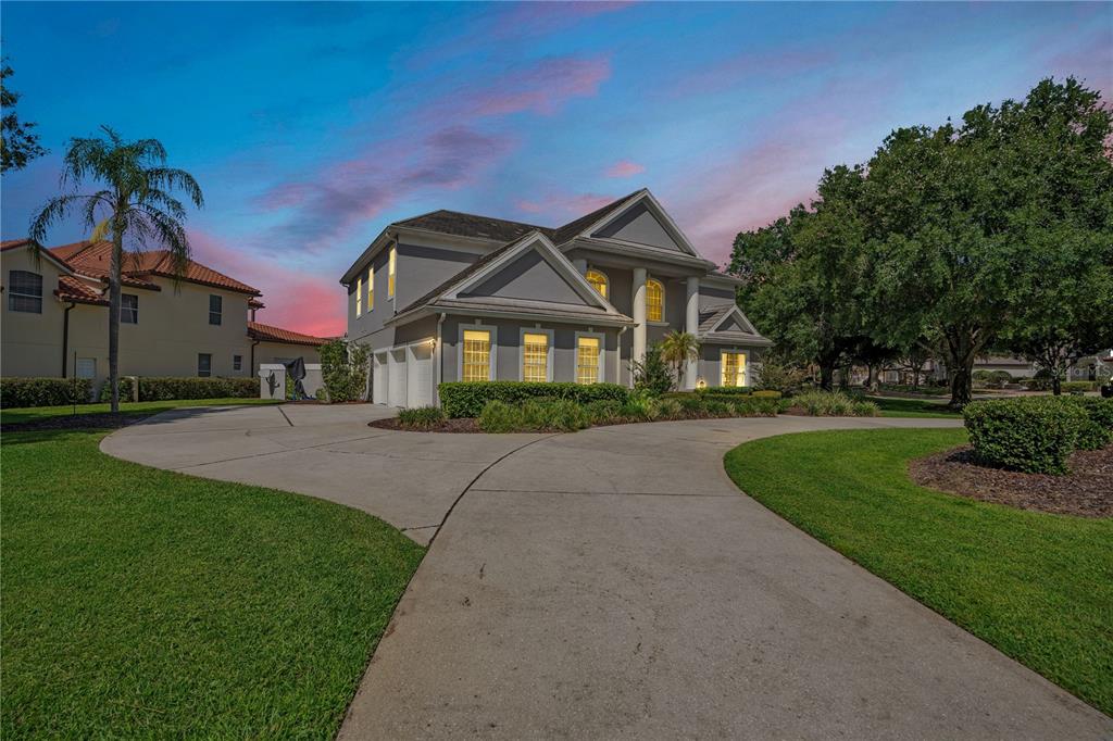 A two-story gray house with a circular driveway and a large front lawn at dusk — 10760 EMERALD CHASE DRIVE, ORLANDO, FL