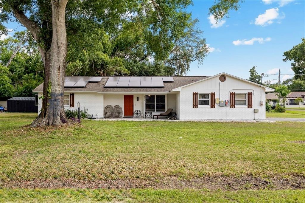A single-story white brick house with a red front door and roof-mounted solar panels — 8212 SUNNY VALE PLACE, TAMPA, FL