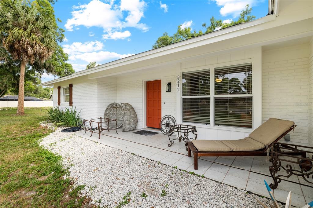 A white brick house exterior features a bright orange front door and a tiled porch — 8212 SUNNY VALE PLACE, TAMPA, FL