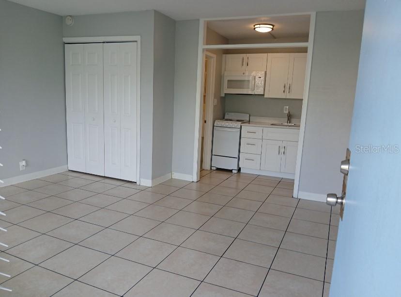 A room with light-colored tile flooring, a white closet, and an adjacent small kitchen area — 515 BON AIR STREET UNIT 130, LAKELAND, FL