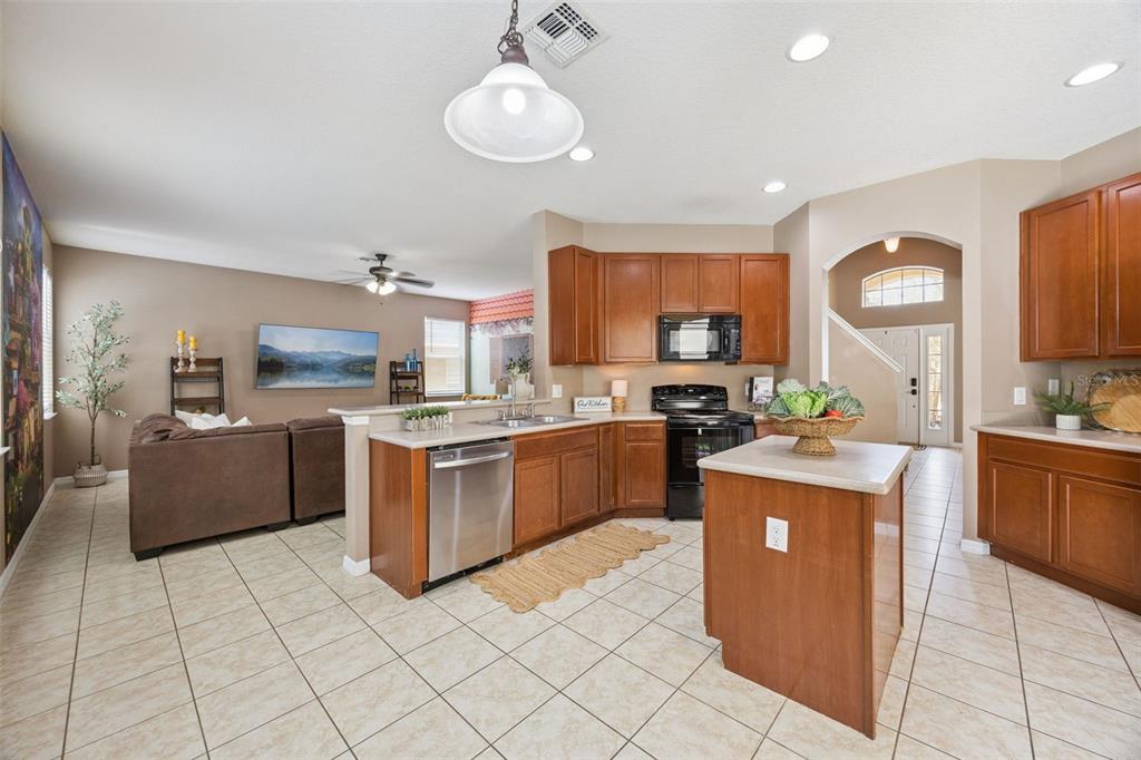 A kitchen with wood cabinets and a stainless steel dishwasher opens to a living area — 4460 NIRVANA PARKWAY, KISSIMMEE, FL