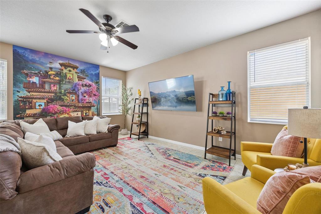 A living room features a brown sectional, yellow armchairs, a colorful rug, and wall art — 4460 NIRVANA PARKWAY, KISSIMMEE, FL