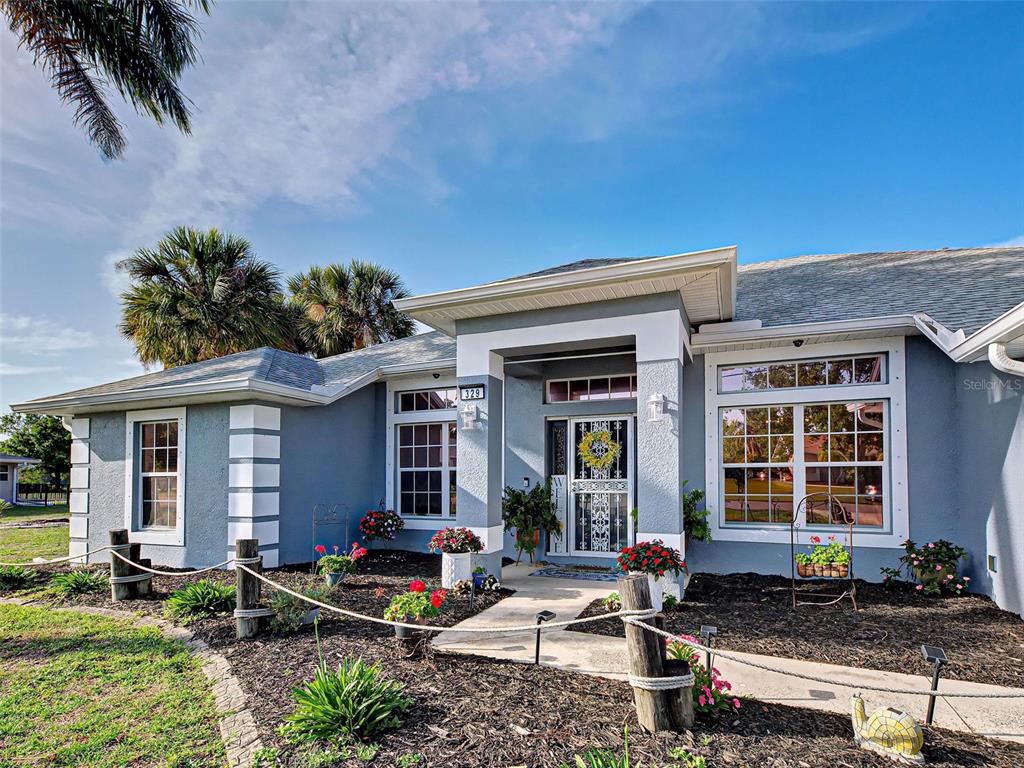 The exterior of a single-story blue house features a front porch and landscaped garden beds — 329 BAHIA BLANCA DRIVE, PUNTA GORDA, FL