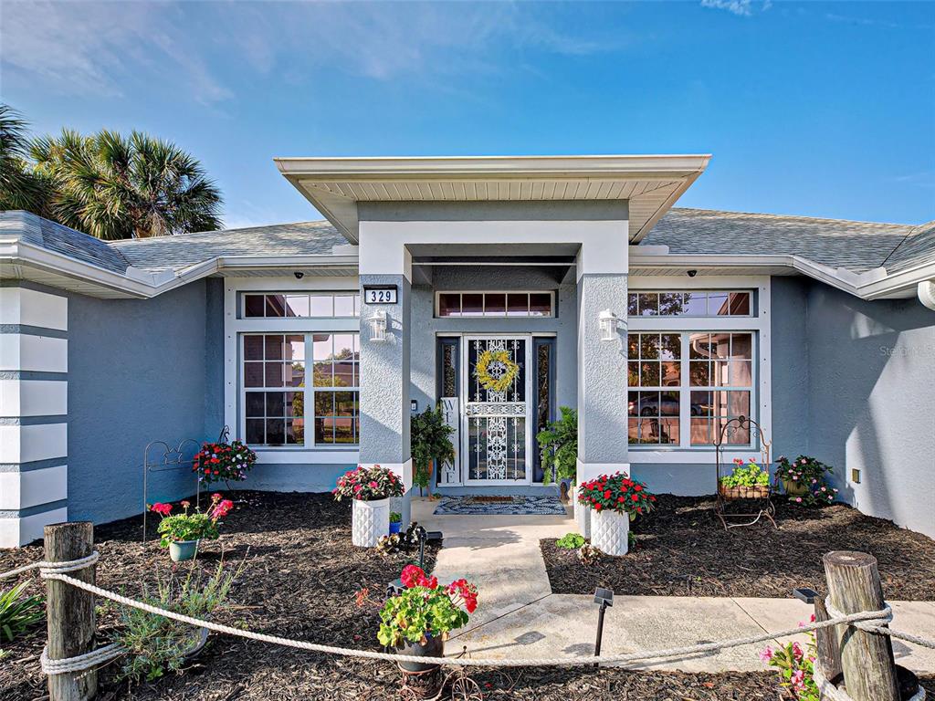 The exterior of a single-story house features a covered entryway, large windows, and landscaped beds — 329 BAHIA BLANCA DRIVE, PUNTA GORDA, FL