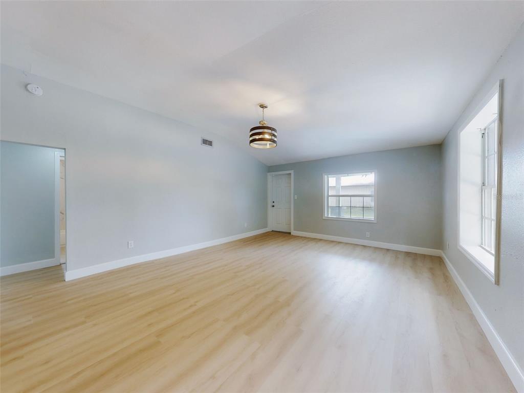An empty room with light wood-look flooring, light gray walls, and a modern drum chandelier — 1103 WASHINGTON STREET, NEW SMYRNA BEACH, FL