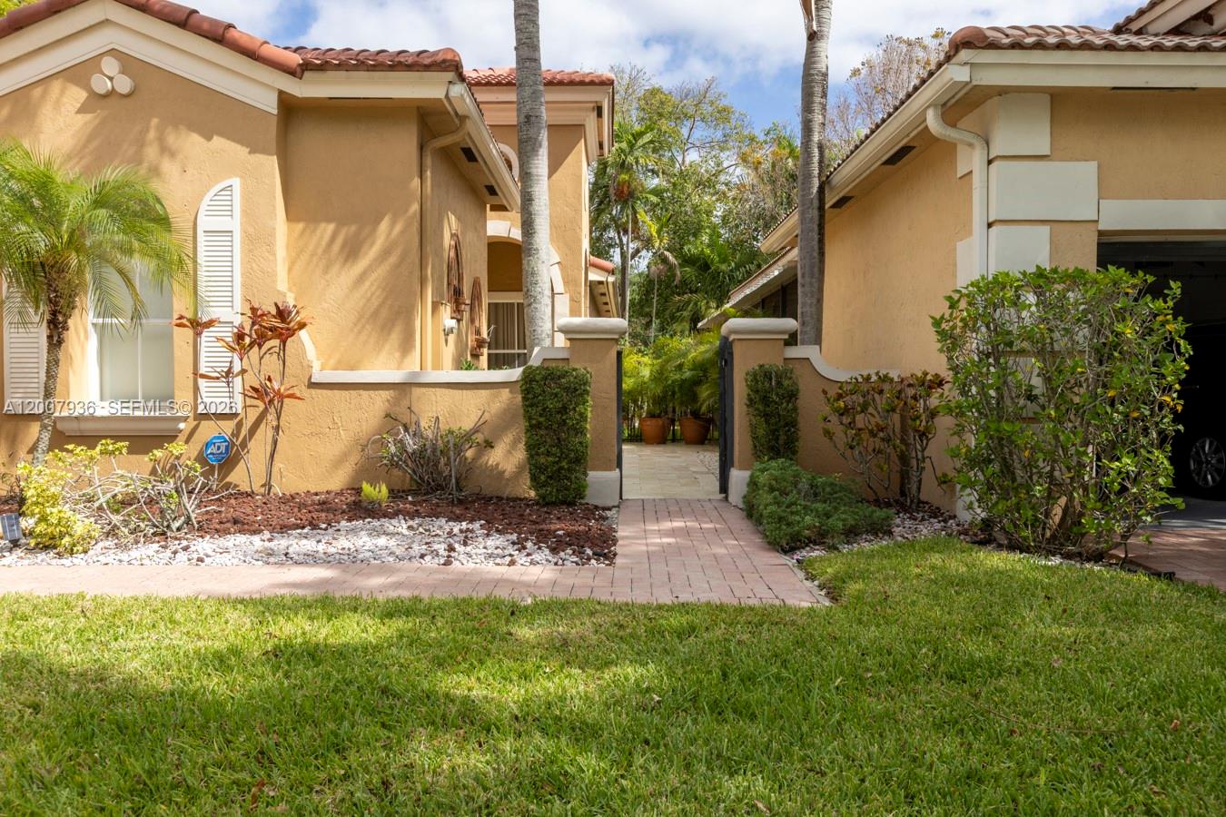 A tan stucco house features a brick walkway leading to a gated courtyard entrance — 12159 NW 59th St, Coral Springs FL 33076, CORAL SPRINGS, FL