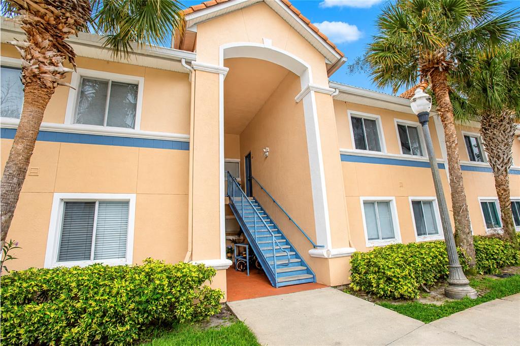 An exterior view of a two-story apartment building with tan stucco walls and blue stairs — 508 VILLA DEL SOL CIRCLE UNIT 204, ORLANDO, FL