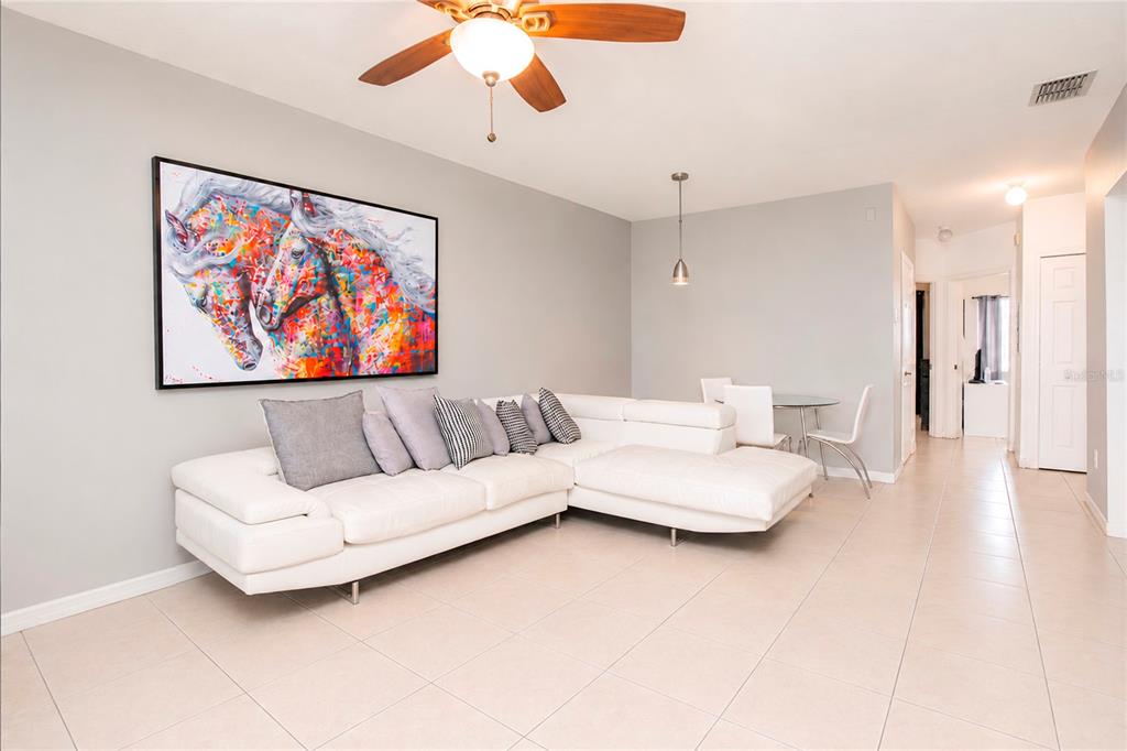A living room features a white sectional sofa, colorful horse artwork, and light tile flooring — 508 VILLA DEL SOL CIRCLE UNIT 204, ORLANDO, FL