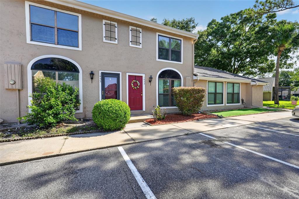 The exterior of a two-story tan townhouse features a red front door and parking spaces — 1453 CASA PARK CIRCLE, WINTER SPRINGS, FL