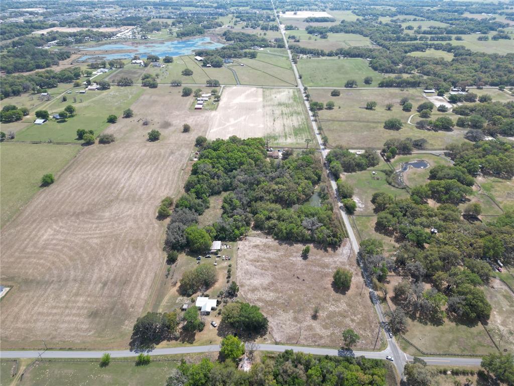 An aerial view shows a rural property with houses, open fields, and wooded areas — 3095 COUNTY ROAD 202, OXFORD, FL
