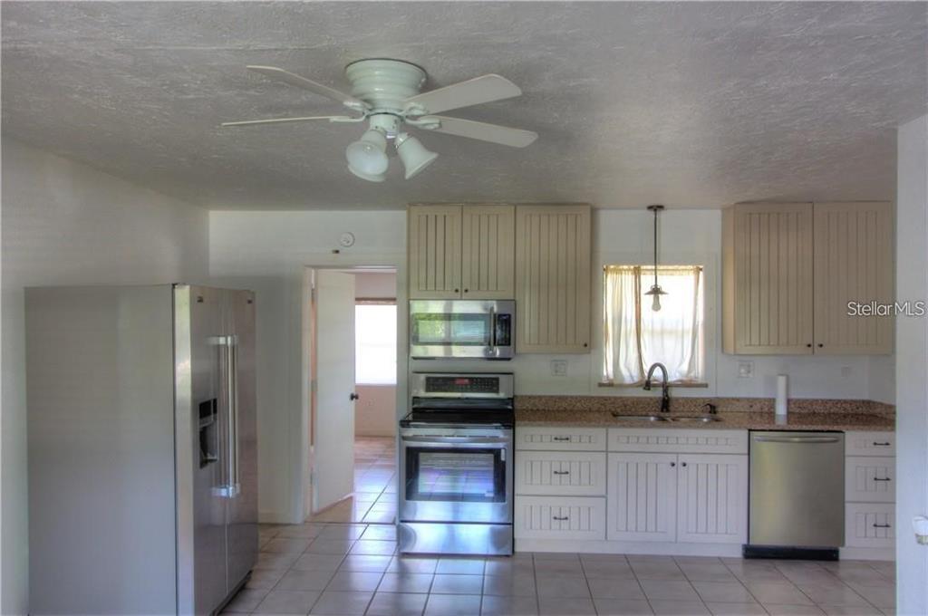 A kitchen features white cabinets, stainless steel appliances, tile flooring, and a ceiling fan — 613 SHORE ROAD, NOKOMIS, FL