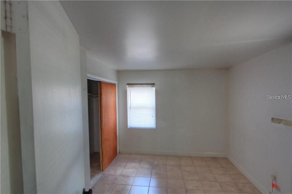 A small, empty bedroom with white walls, tiled flooring, and a sliding wooden closet door — 613 SHORE ROAD, NOKOMIS, FL