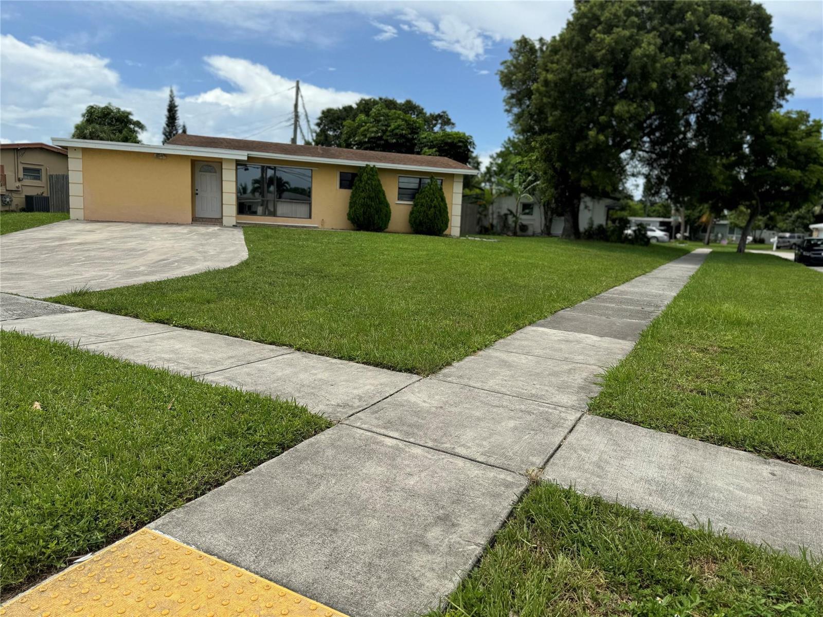 A yellow single-story house with a concrete driveway and sidewalk sits on a grassy lot — 6101 NW 18th Street, Margate FL 33063, MARGATE, FL