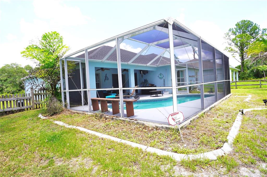 A swimming pool is enclosed by a screen cage behind a house with a yard — 2376 DODGE STREET, PORT CHARLOTTE, FL