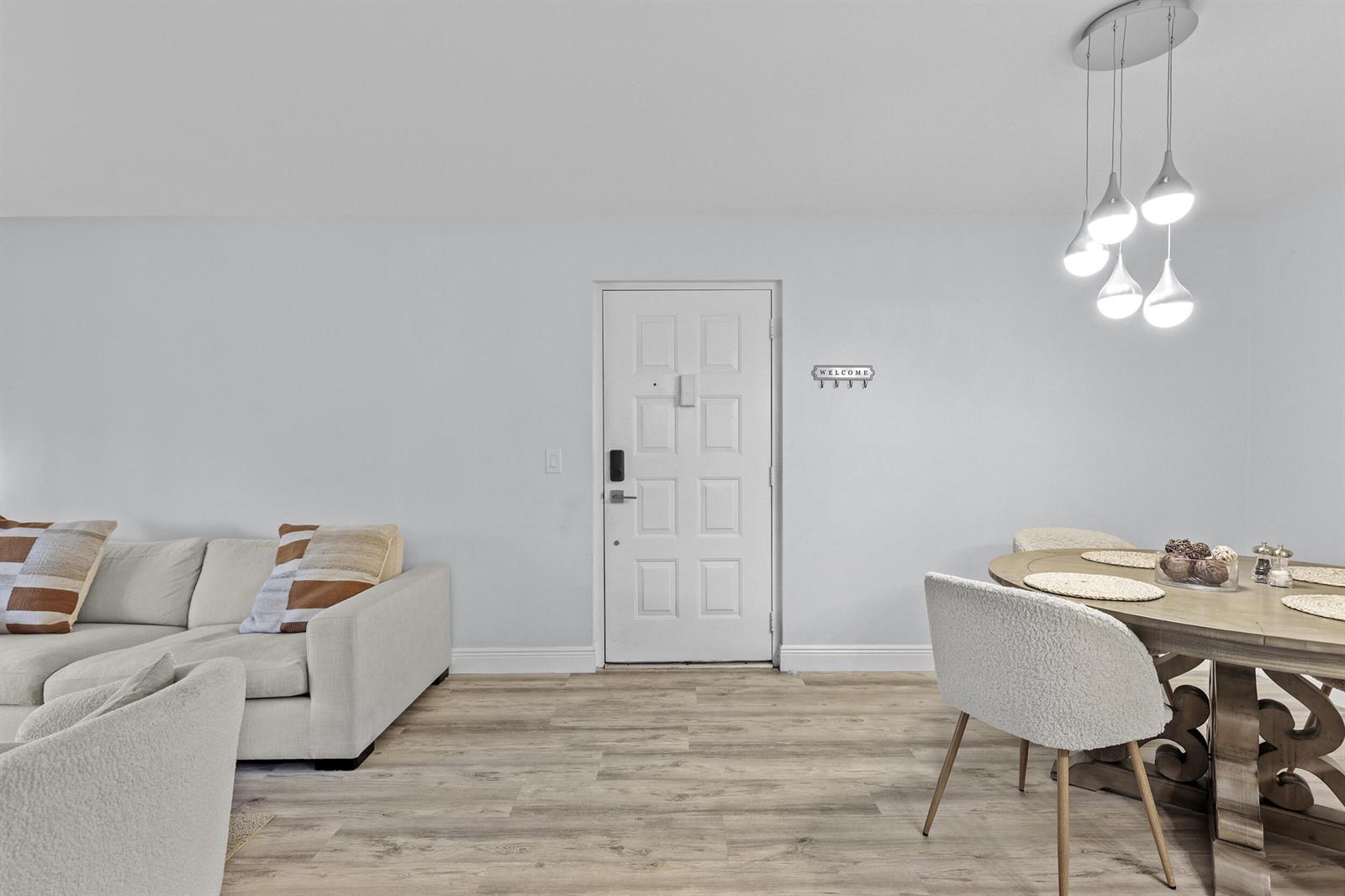 A living and dining area features light wood flooring, a white door, and modern pendant lighting — 629 Sea Pine Way # D2, FL 33415, FL