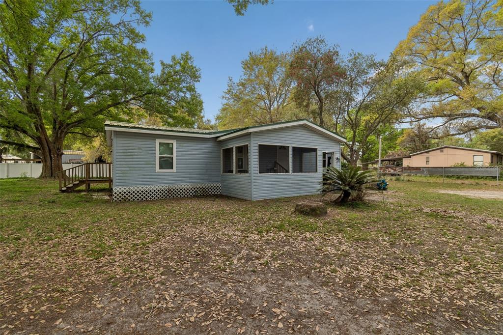 A light blue single-story house with a screened-in porch sits on a grassy, tree-filled lot — 4505 ESTATE DRIVE, PLANT CITY, FL