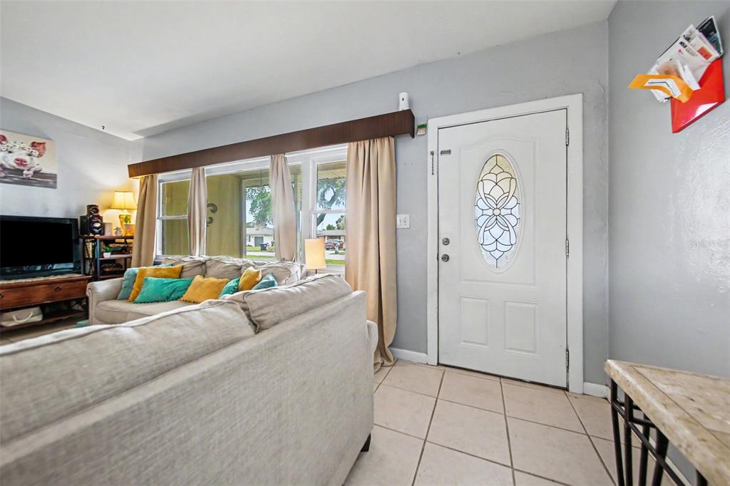 A living room features a beige sofa, tiled floors, a front door, and large windows — 1909 JASPER DRIVE, ORLANDO, FL