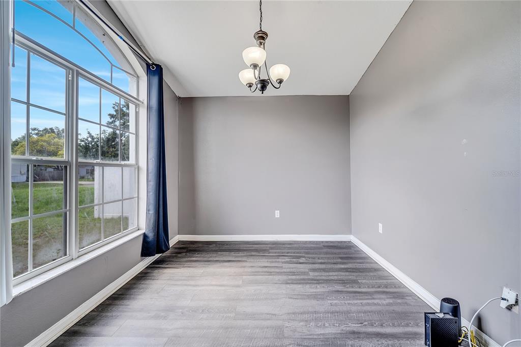 An empty room with gray walls, dark wood-look flooring, a chandelier, and a large window — 9821 8TH AVENUE, ORLANDO, FL