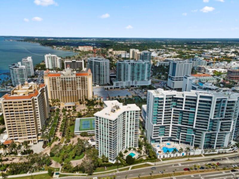 An aerial view of multiple high-rise apartment buildings and a tennis court near a bay — 1111 N GULFSTREAM AVENUE UNIT 5B, SARASOTA, FL