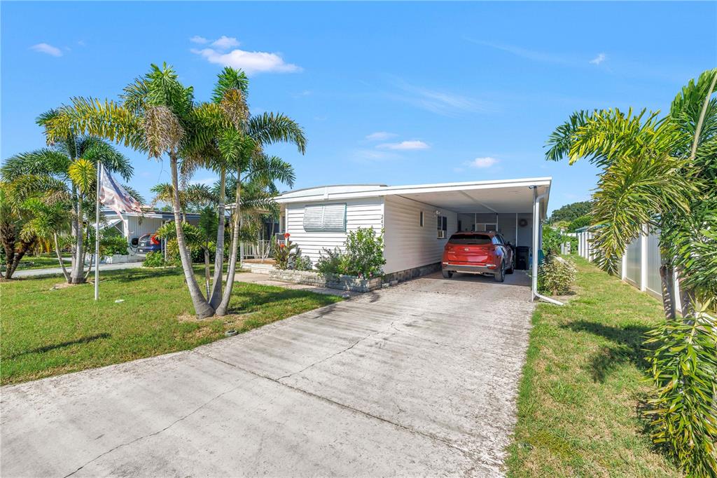 A single-story mobile home features a concrete driveway, a carport, and several palm trees — 2439 SANTIAGO DRIVE, HOLIDAY, FL
