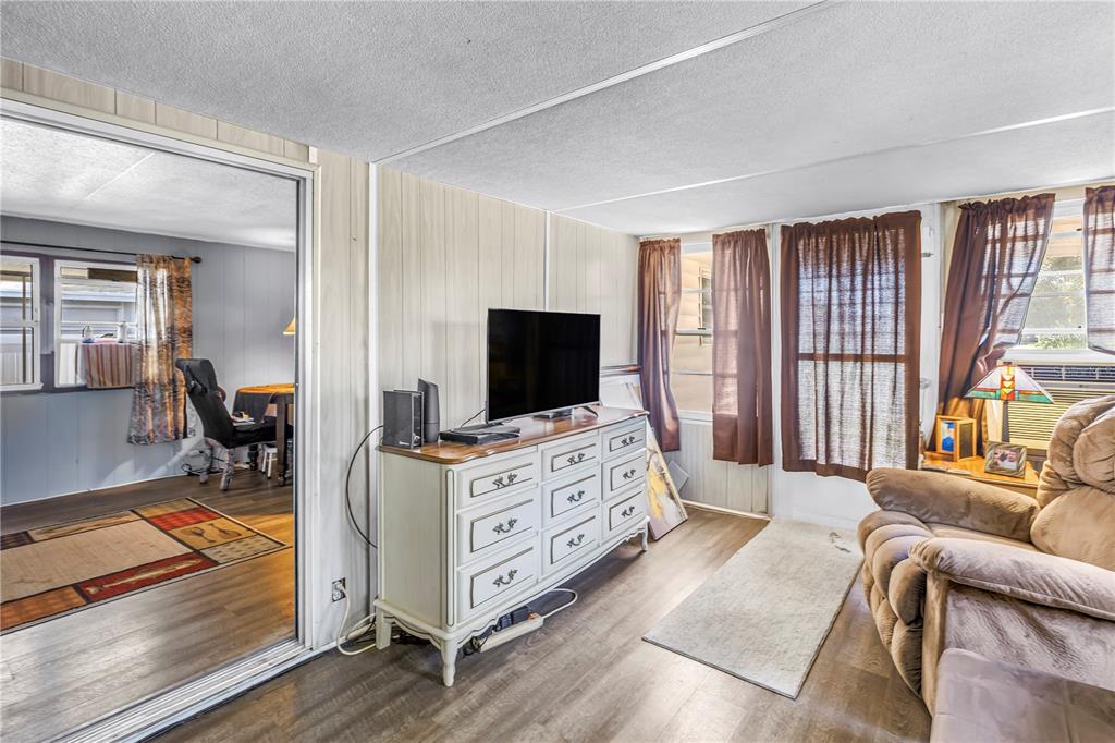 A living room features wood-look flooring, a white dresser with a television, and a recliner — 2439 SANTIAGO DRIVE, HOLIDAY, FL