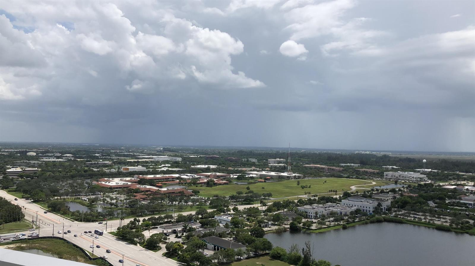 An aerial view shows a suburban landscape with office buildings, green spaces, and a lake — 2000 Metropica Way # 1609, Sunrise FL 33323, SUNRISE, FL