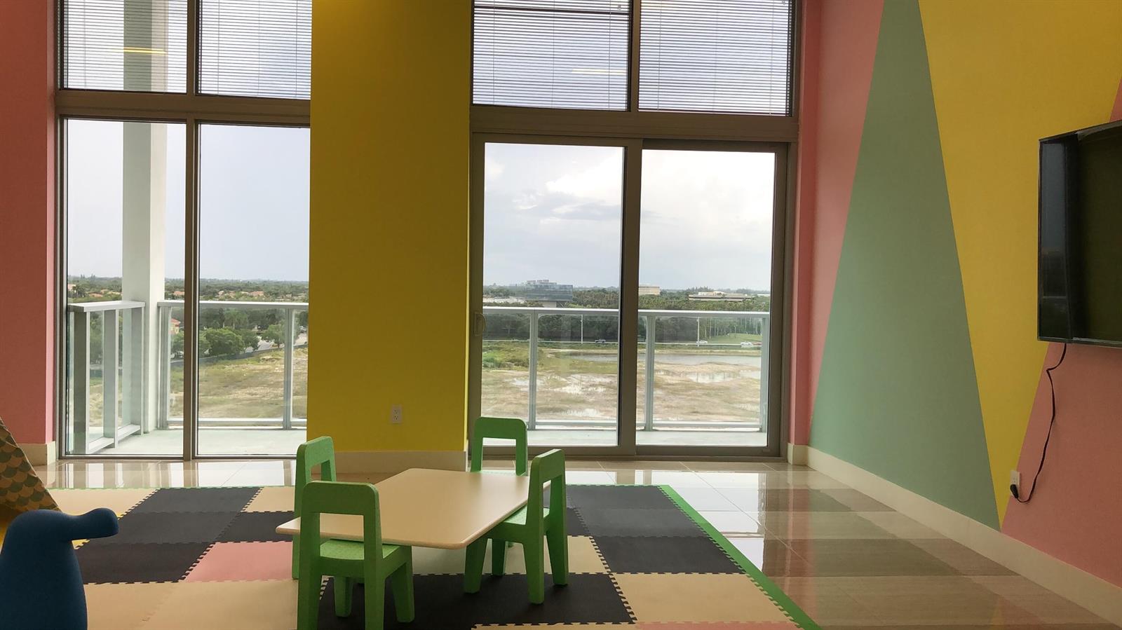 A colorful playroom features a small table with chairs, floor mats, and large glass windows — 2000 Metropica Way # 1609, Sunrise FL 33323, SUNRISE, FL