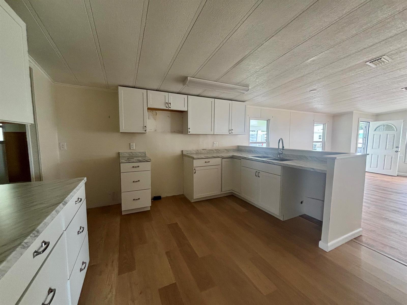 A kitchen features white cabinets, light countertops, and wood-look flooring in an open floor plan — 1745 SW 35th Circle, Okeechobee FL 34974, OKEECHOBEE, FL