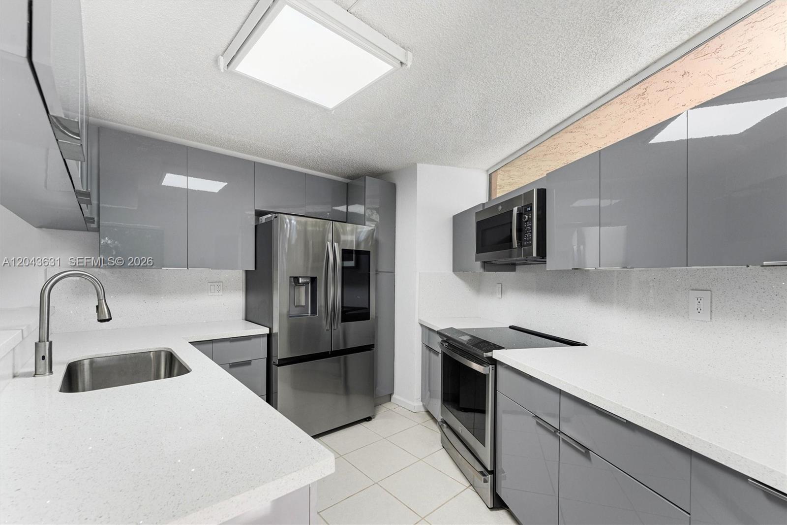 A modern kitchen features gray glossy cabinets, stainless steel appliances, and white quartz countertops — 8111 Severn Dr # D, Boca Raton FL 33433, BOCA RATON, FL