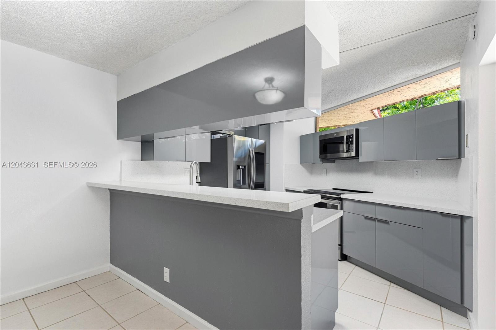 A kitchen features gray cabinets, white countertops, and a breakfast bar with tile flooring — 8111 Severn Dr # D, Boca Raton FL 33433, BOCA RATON, FL