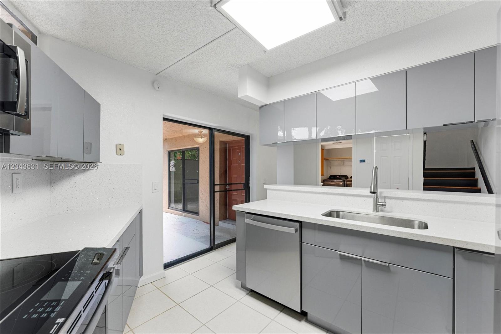 A modern kitchen features gray cabinets, white countertops, stainless steel appliances, and a sliding glass door — 8111 Severn Dr # D, Boca Raton FL 33433, BOCA RATON, FL
