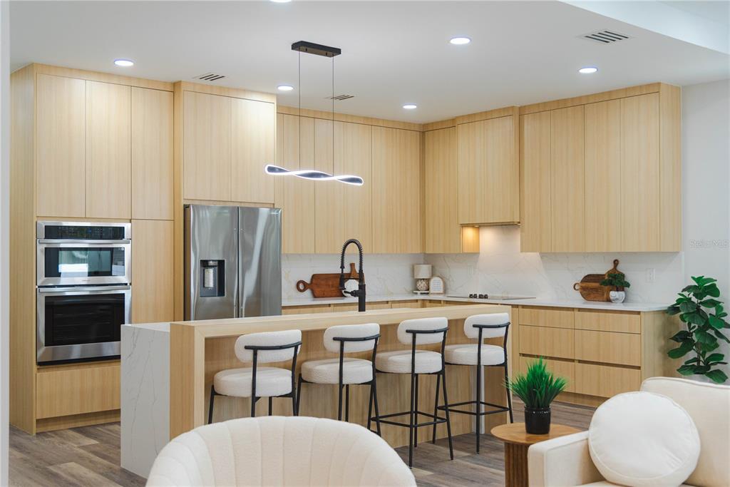 A modern kitchen features light wood cabinetry, a waterfall island with bar seating, and stainless appliances — 2714 W TAMPA BAY BOULEVARD, TAMPA, FL