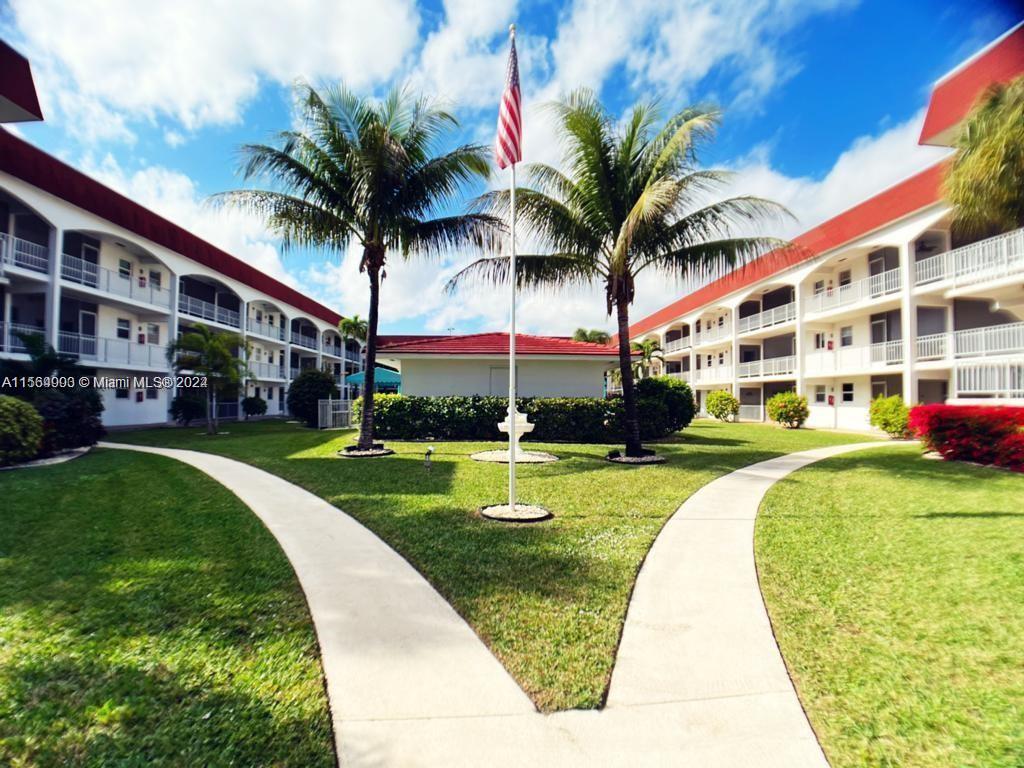 A courtyard with a flagpole, palm trees, and walkways between two multi-story apartment buildings — 580 Egret Dr # 302, Hallandale Beach FL 33009, HALLANDALE BEACH, FL