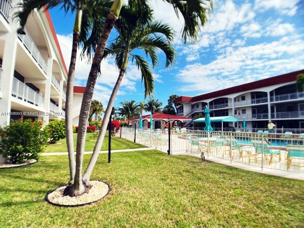 A swimming pool area with palm trees, lounge chairs, and multi-story apartment buildings — 580 Egret Dr # 302, Hallandale Beach FL 33009, HALLANDALE BEACH, FL