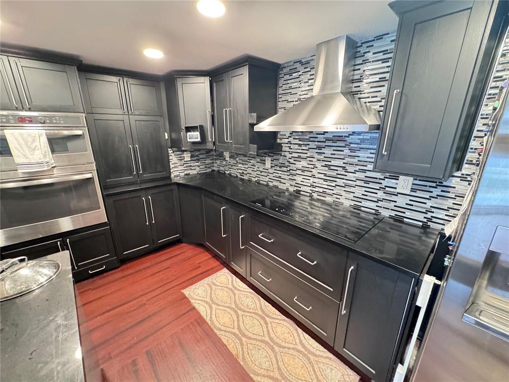 A kitchen features dark cabinetry, black countertops, a stainless steel range hood, and wood flooring — 12555 BROOKSIDE STREET, SPRING HILL, FL