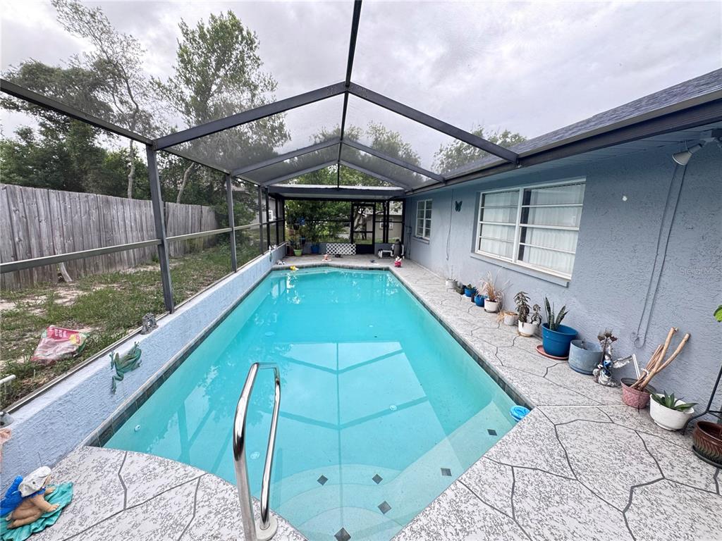 A screened-in swimming pool with a concrete deck sits beside a blue house exterior — 12555 BROOKSIDE STREET, SPRING HILL, FL