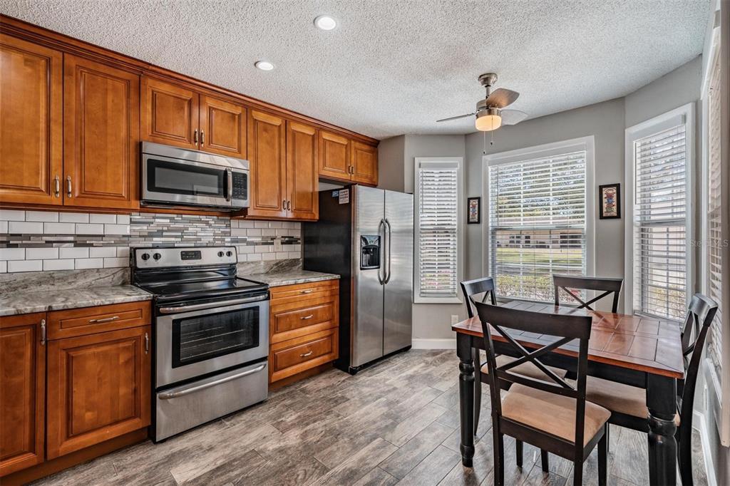 A kitchen features wood cabinets, stainless steel appliances, a tile backsplash, and a dining area — 11308 VERSAILLES LANE UNIT C, PORT RICHEY, FL