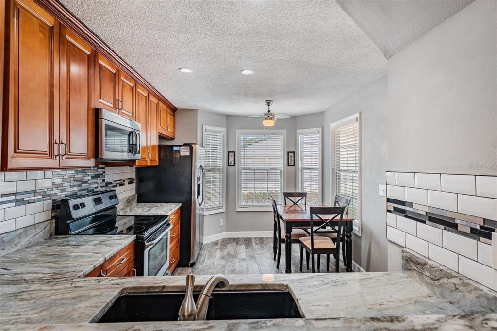 A kitchen with wood cabinets, granite countertops, a black sink, and a dining area — 11308 VERSAILLES LANE UNIT C, PORT RICHEY, FL