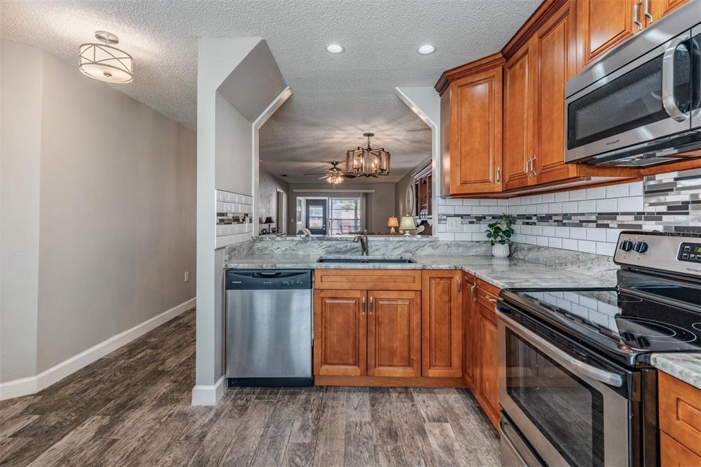 A kitchen with wood cabinets, stainless steel appliances, and a pass-through window to the living area — 11308 VERSAILLES LANE UNIT C, PORT RICHEY, FL