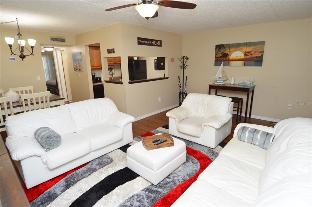 A living room with white sofas, a television, and an open kitchen pass-through window — 12760 INDIAN ROCKS ROAD UNIT 1030 (Furnished), LARGO, FL