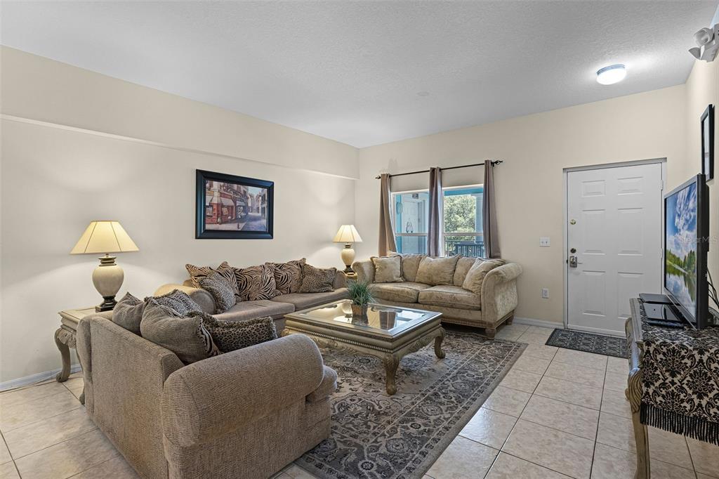 A living room features beige tile floors, two tan sofas, a coffee table, and a television — 3111 SUN LAKE COURT UNIT B, KISSIMMEE, FL