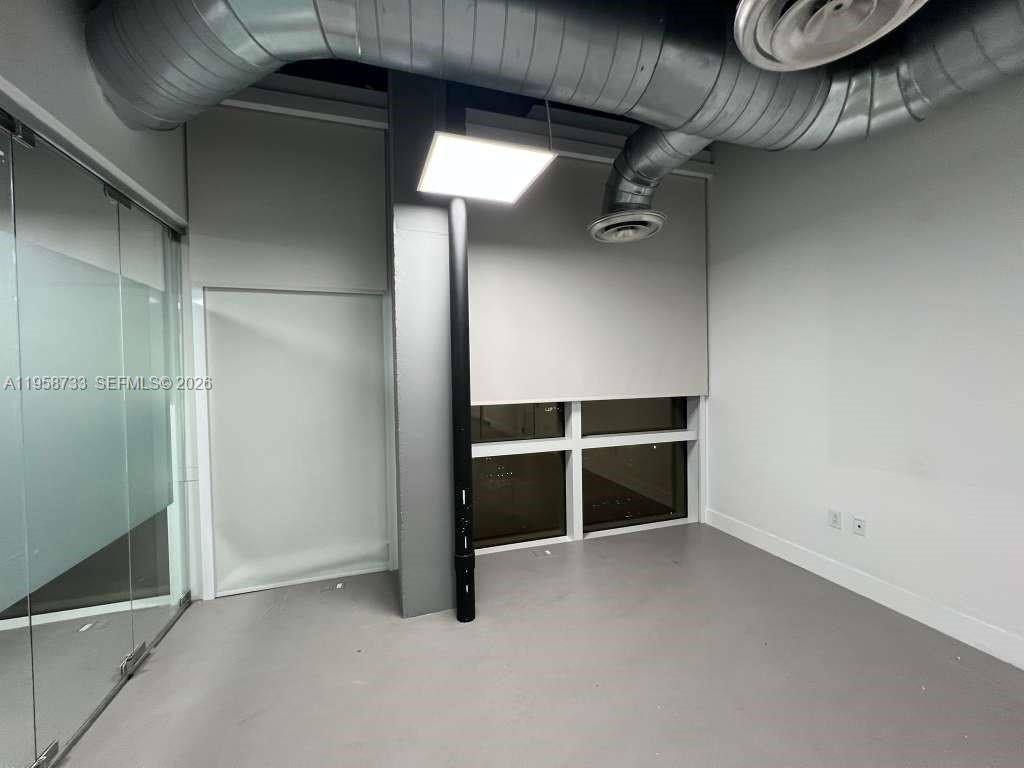 An office space features gray flooring, exposed ductwork, a square ceiling light, and glass walls — 20200 W Dixie Hwy # 1008, Miami FL 33180, MIAMI, FL