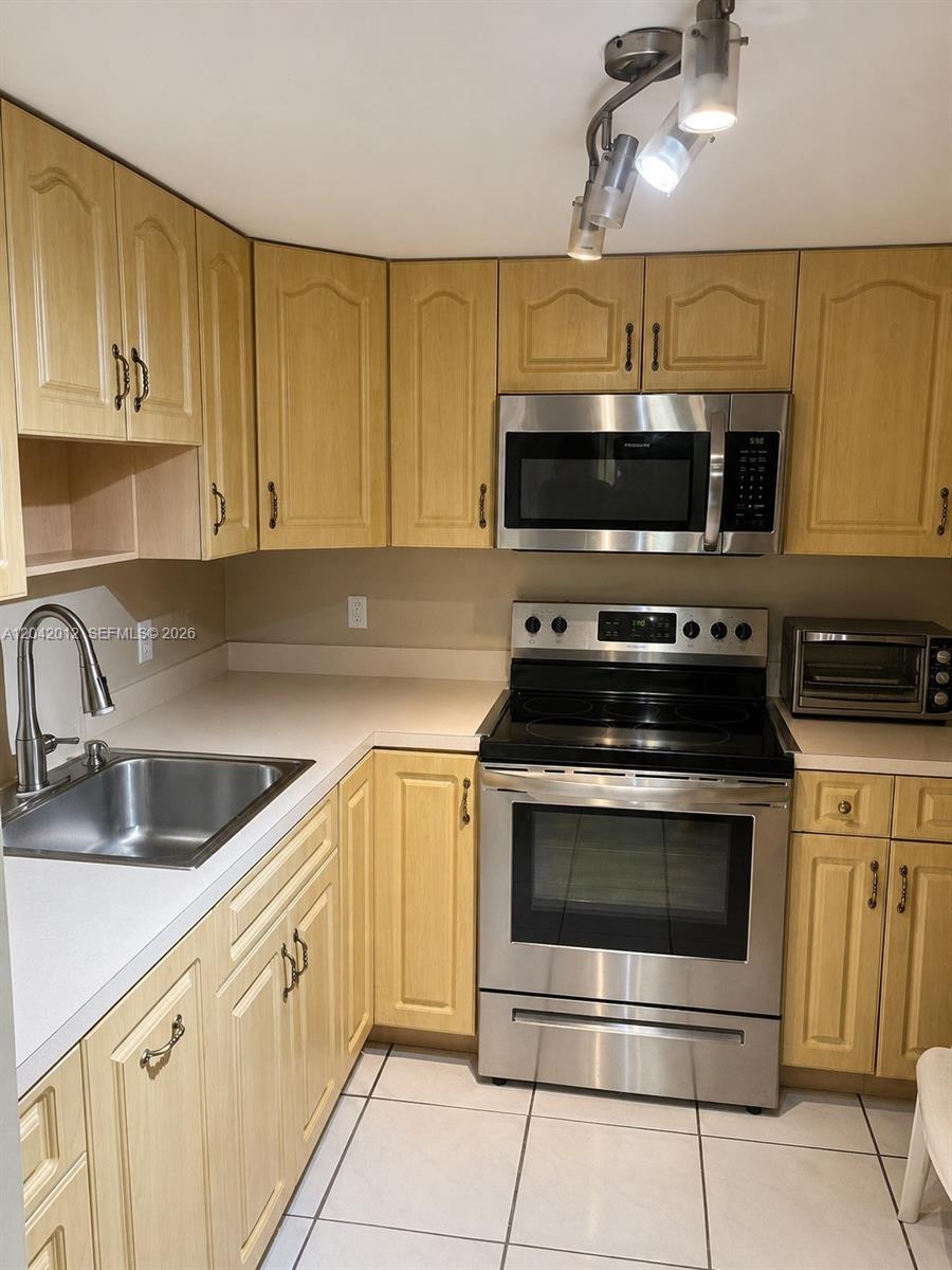 A kitchen features light wood cabinets, stainless steel appliances, and white tile flooring — 2055 SW 122nd Ave # 321, Miami FL 33175, MIAMI, FL